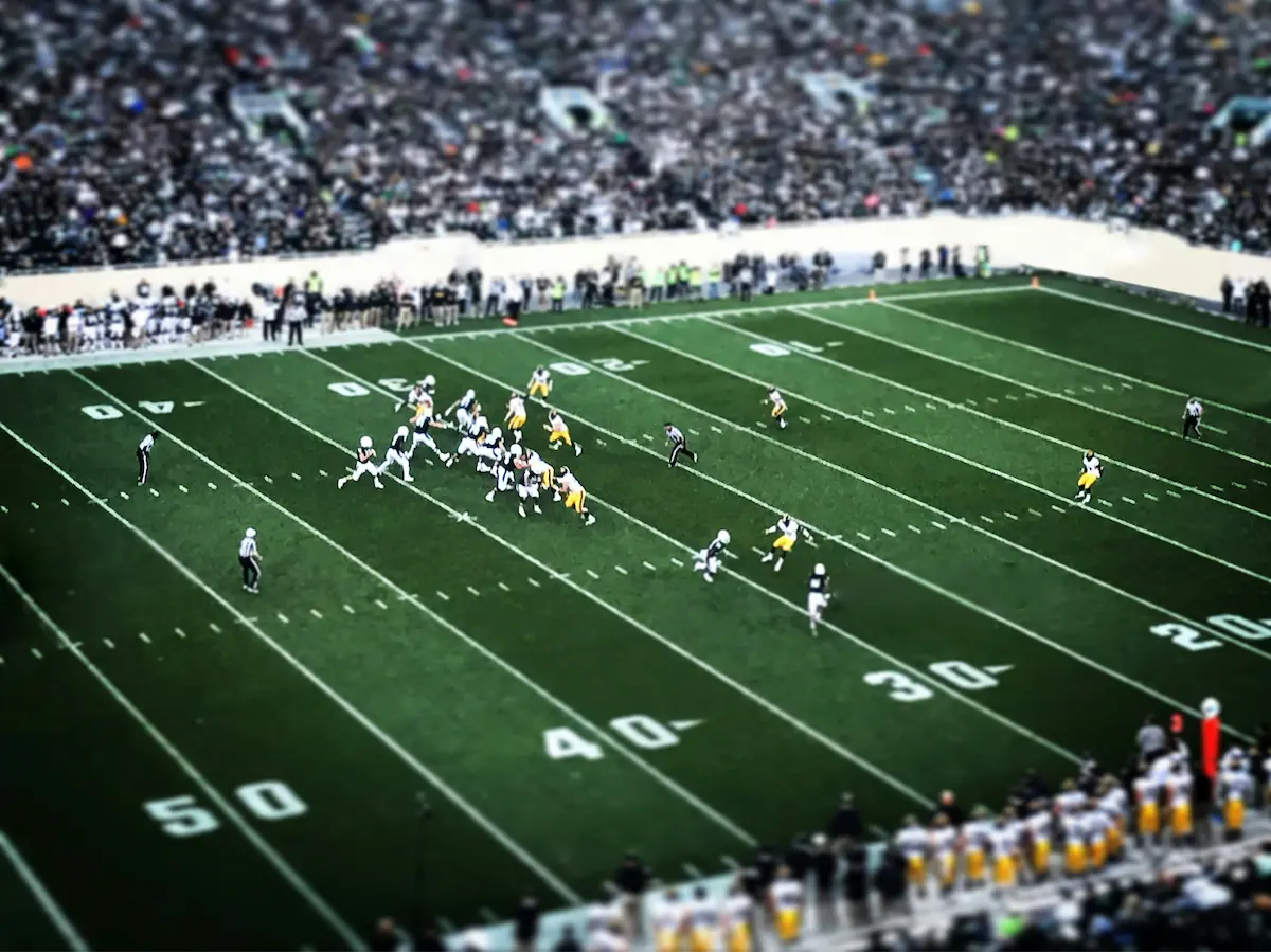 A football game, mid-play, in a packed stadium of cheering fans.